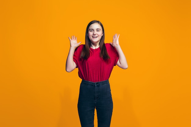 La niña adolescente feliz de pie y sonriendo contra el espacio naranja.