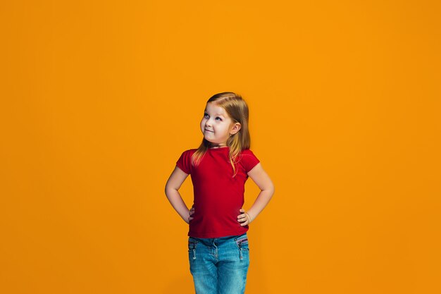 La niña adolescente feliz de pie y sonriendo contra el espacio naranja.