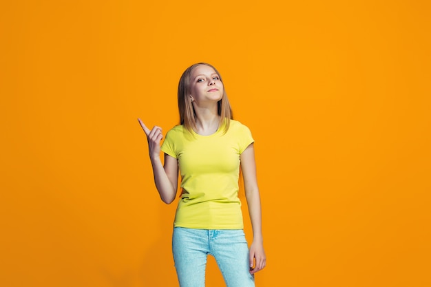 Foto gratuita la niña adolescente feliz de pie y sonriendo contra el espacio naranja.