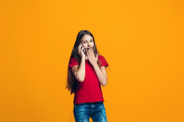 La niña adolescente feliz de pie y sonriendo contra el espacio naranja.