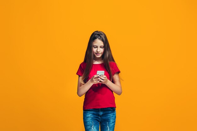 La niña adolescente feliz de pie y sonriendo contra el espacio naranja.