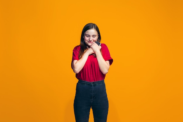 La niña adolescente feliz de pie y sonriendo contra la pared naranja