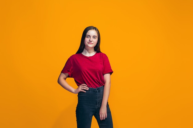 La niña adolescente feliz de pie y sonriendo contra la pared naranja