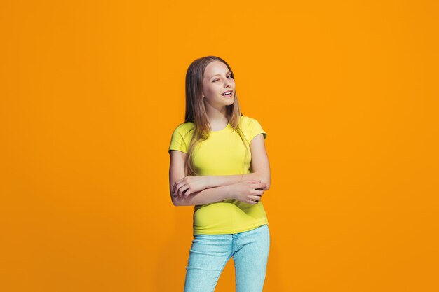 La niña adolescente feliz de pie y sonriendo contra la pared naranja