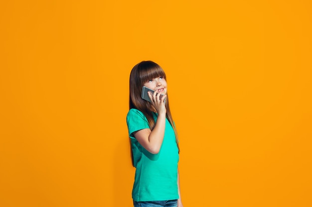 La niña adolescente feliz de pie y sonriendo contra la pared naranja