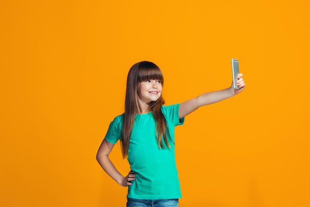 La niña adolescente feliz de pie y sonriendo contra la pared naranja