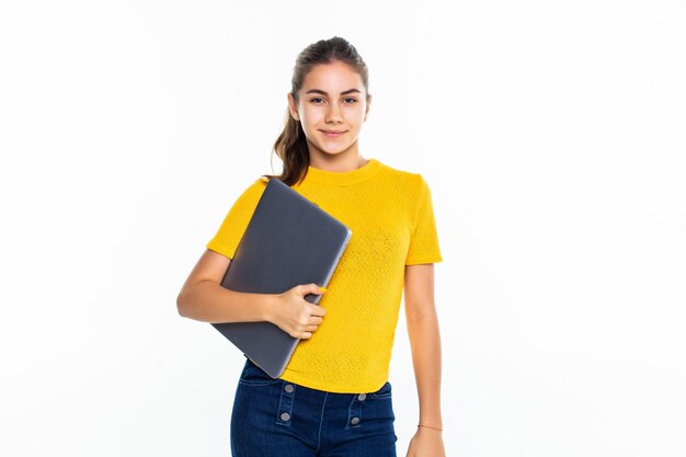 Niña adolescente linda sonriente que usa la computadora portátil sobre la pared blanca