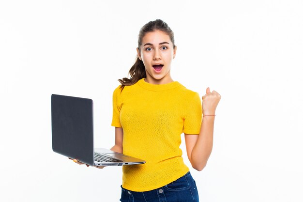 Niña adolescente linda sonriente que usa la computadora portátil sobre la pared blanca