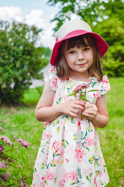 Niña adorable con un ramo de flores silvestres y un sombrero rosa