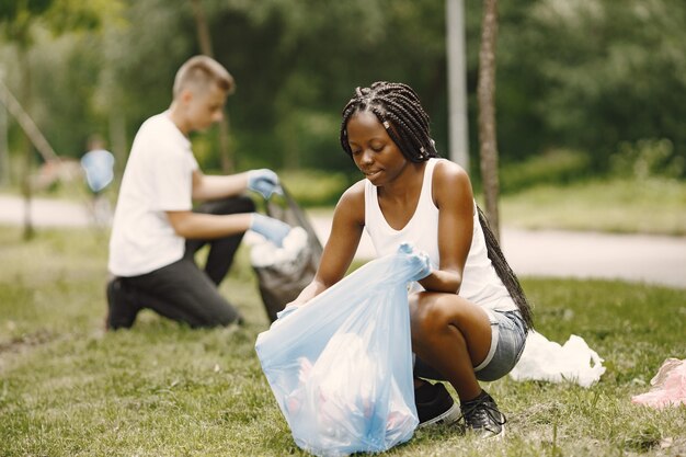 Niña africana y niño europeo pivotando basura. Activistas despejando el parque de lado.