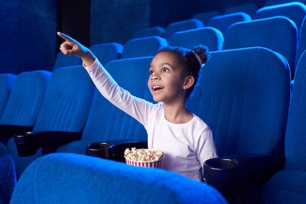 Niña africana poiniting con el dedo en la pantalla en el cine.