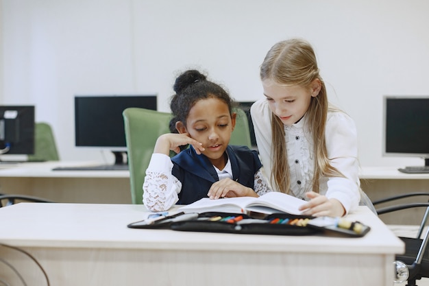 Foto gratuita niña africana sentada en la mesa. las colegialas leen un libro durante un descanso. los niños se sientan en una clase de informática.