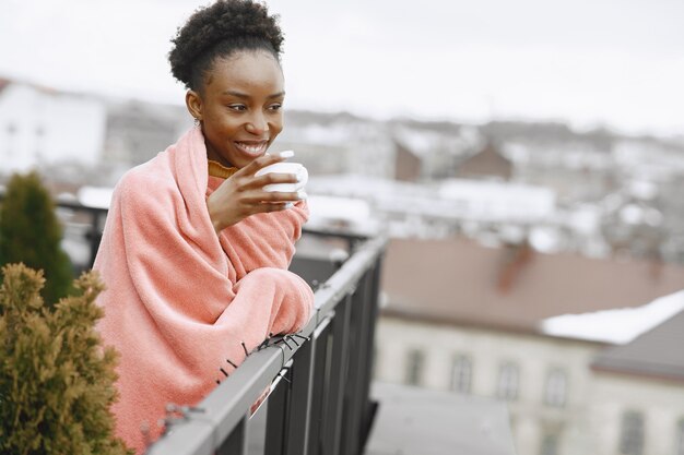 Niña africana en la terraza. Mujer tomando café en una tela escocesa rosa. Señora posando para una foto.