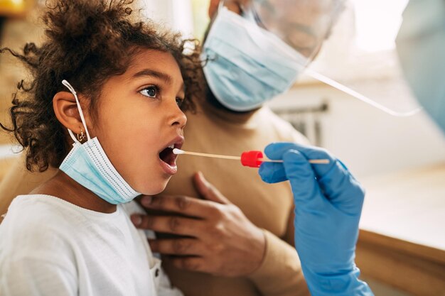 Niña afroamericana durante el examen médico con hisopo en el consultorio del médico