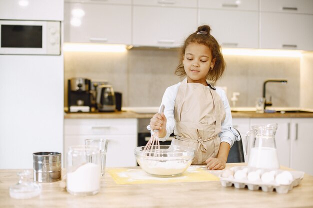 Niña afroamericana mezclando la masa en un recipiente de vidrio, preparando un pastel.