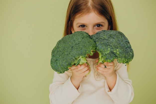 Niña aislada sosteniendo brócoli crudo verde