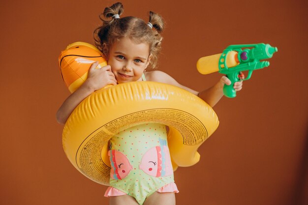 Niña aislada con traje de baño y tubo de goma y pistola de agua en la mano