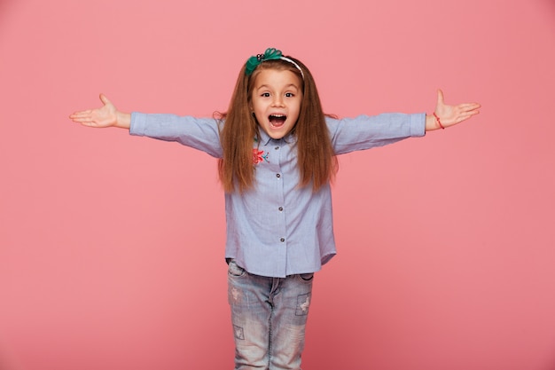 Niña alegre en aro de pelo posando con las manos abiertas siendo amable y acogedor