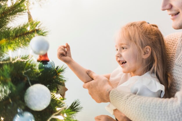 Niña alegre decorando árbol de navidad iluminado
