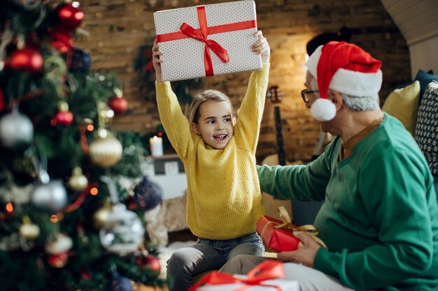 Niña alegre divirtiéndose en Navidad mientras recibe un regalo del abuelo