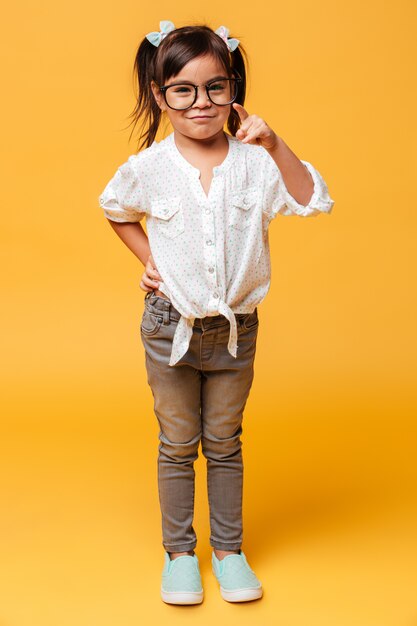 Niña alegre con gafas apuntando a usted.