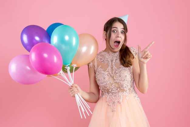 niña alegre con gorro de fiesta sosteniendo globos en rosa