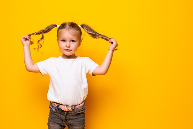 Niña alegre jugando con el pelo posando aislado en la pared amarilla