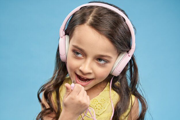 Niña alegre posando, con auriculares de color rosa.