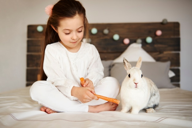 Foto gratuita niña alimentando a su conejo en la cama