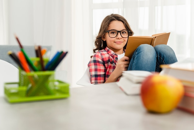 Niña de ángulo bajo en casa leyendo