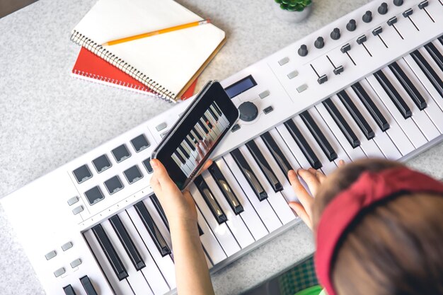 Una niña aprende a tocar el piano con una lección de música en línea para teléfonos inteligentes