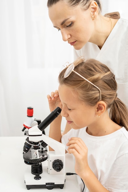 Niña aprendiendo a mirar en el microscopio con maestra