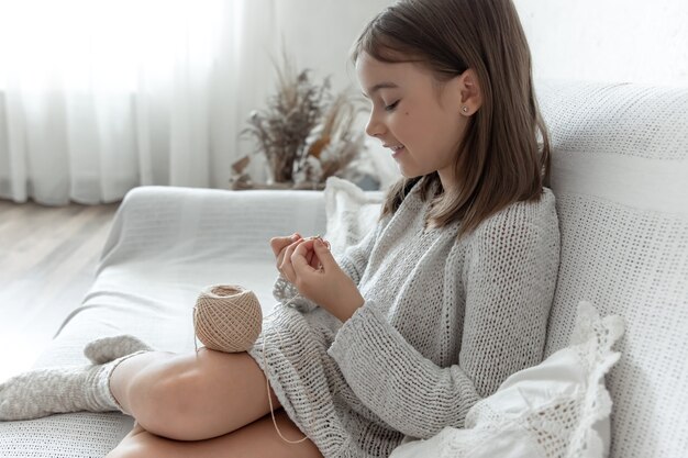 Niña aprendiendo a tejer, ocio en casa y concepto de costura.