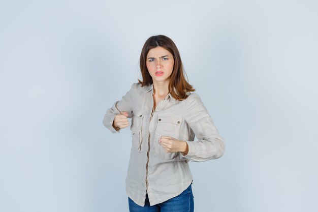 Niña apretando los puños, haciendo muecas en camisa beige, jeans y con enojo. vista frontal.