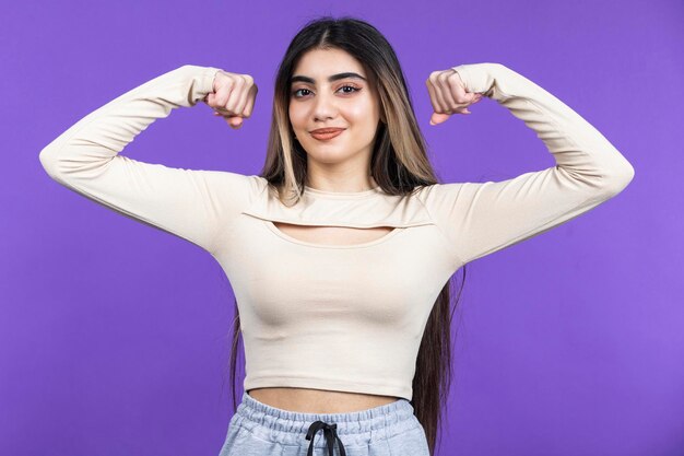 Niña apretando sus bíceps y sonriendo a la cámara Foto de alta calidad