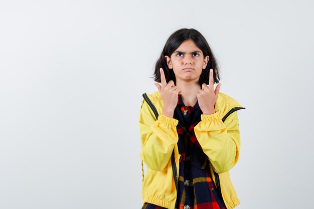 Niña apuntando hacia arriba en camisa a cuadros, chaqueta y mirando vacilante