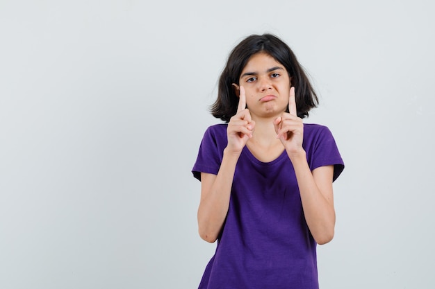 Niña apuntando hacia arriba en camiseta y mirando abatido.