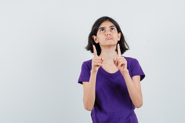 Niña apuntando hacia arriba en camiseta y mirando dudoso