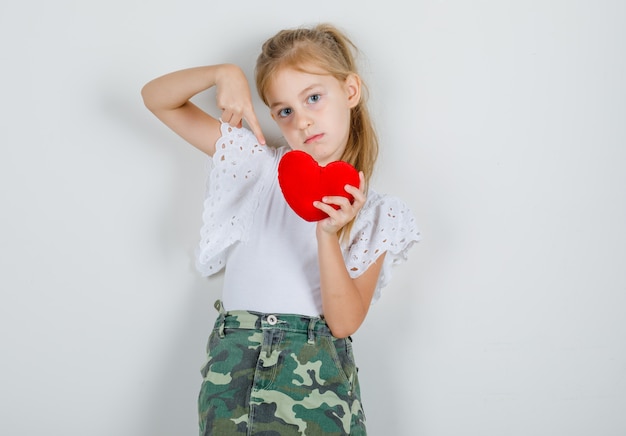 Niña apuntando con el dedo al corazón rojo en camiseta blanca