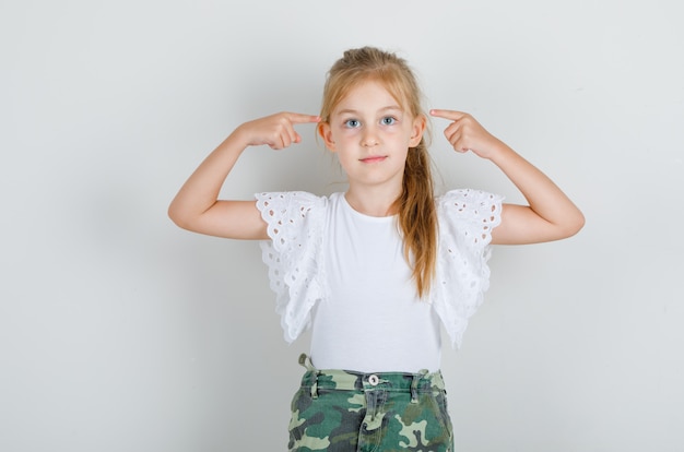 Niña apuntando con el dedo a las sienes en camiseta blanca