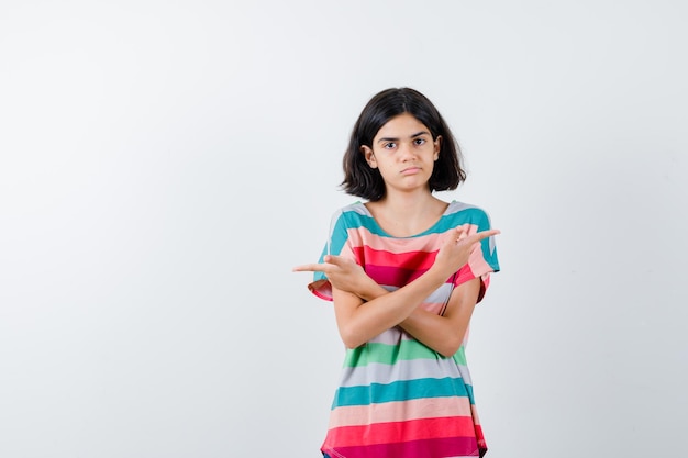 Foto gratuita niña apuntando en direcciones opuestas con los dedos índices en una camiseta a rayas de colores y luciendo linda vista frontal.