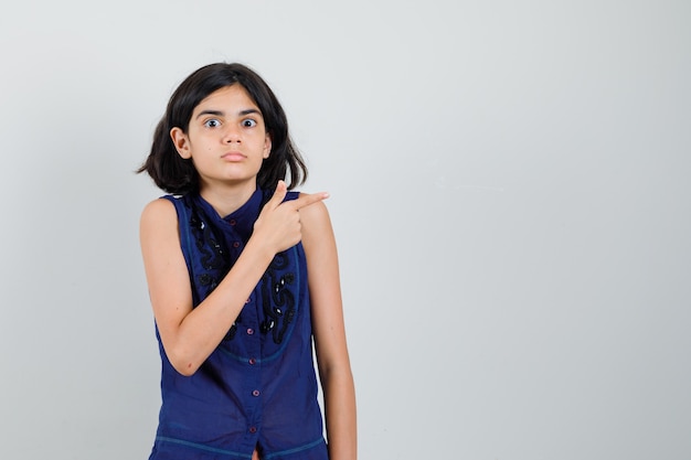 Niña apuntando hacia el lado en blusa azul y mirando desconcertado