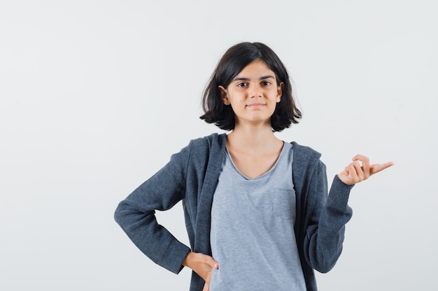 Foto gratuita niña apuntando a un lado en camiseta, chaqueta y mirando confiada.