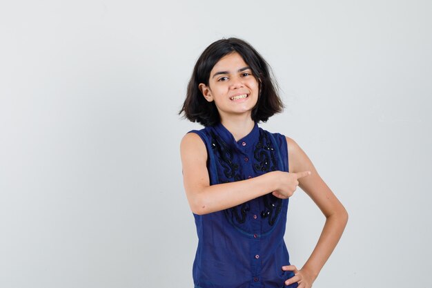 Niña apuntando hacia el lado derecho en blusa azul y mirando feliz.