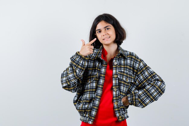 Niña apuntando a su sonrisa en camisa, chaqueta y mirando contenta. vista frontal.