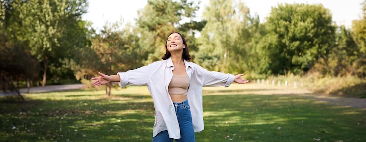 Foto gratuito niña asiática despreocupada riendo y bailando en el parque disfrutando del soleado día de verano levantando las manos y