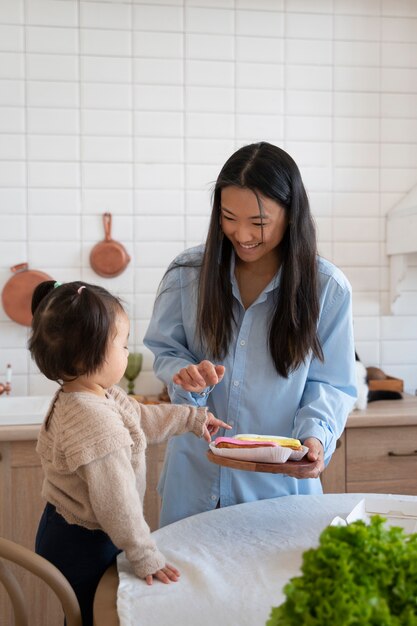 Niña asiática gastando en casa en la cocina con su madre