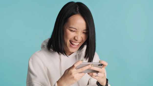 Niña asiática jugando emocionalmente en el teléfono inteligente en un juego en línea aislado en un fondo colorido Expresión facial alegre