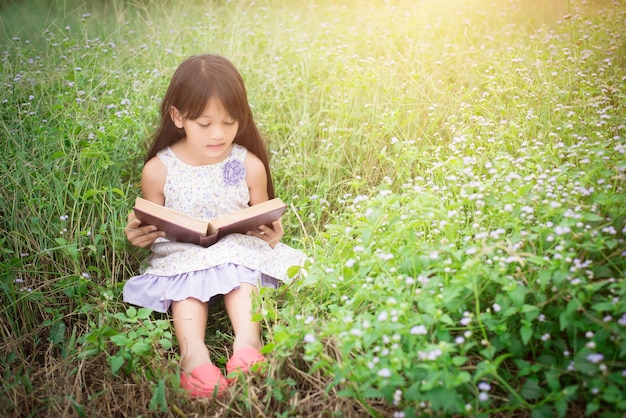 Niña asiática linda leyendo el libro en la naturaleza.