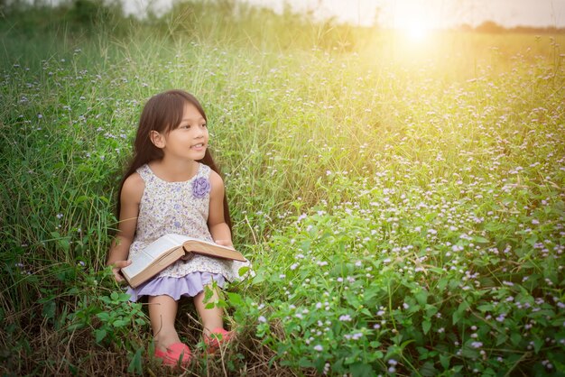 Niña asiática linda leyendo el libro en la naturaleza.